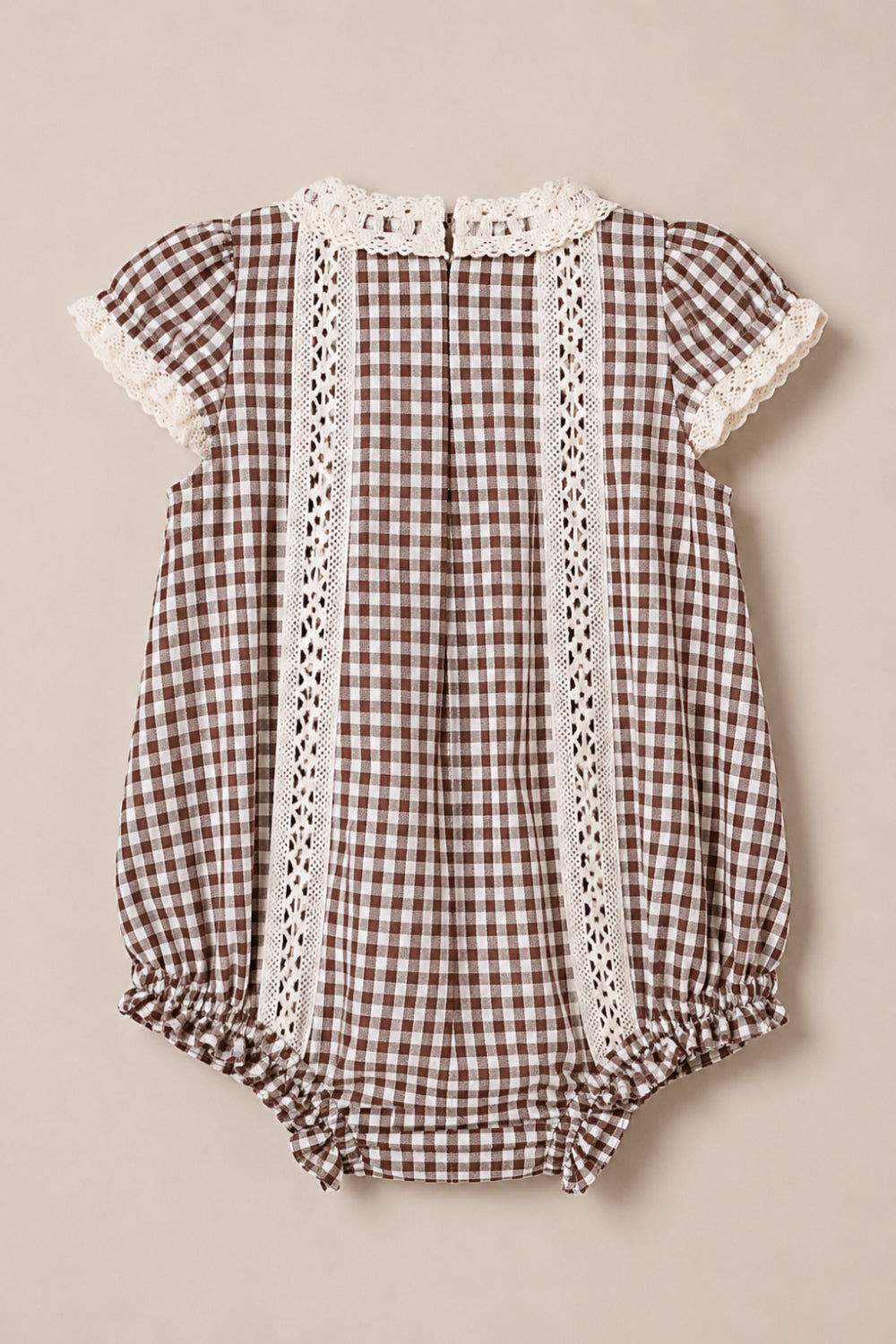 The Ivy City Co Baby Palermo Romper in Hickory Gingham features a charming brown and white gingham pattern, short sleeves, delicate lace trim on the sleeves and collar, vertical lace accents down the front, gathered leg openings, and convenient snap closures at the bottom—all crafted from a soft cotton-blend for all-day comfort.