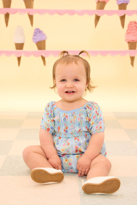 a baby wearing a blue floral baby romper sitting on the a tiled floor in front of an ice cream wall
