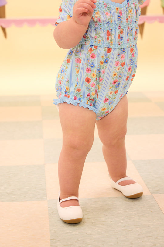 the bottom half a baby wearing a blue floral baby romper standing on the a tiled floor in front of an ice cream wall