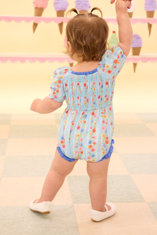 Child in a colorful romper standing on a checkered floor with ice cream cone decorations in the background.