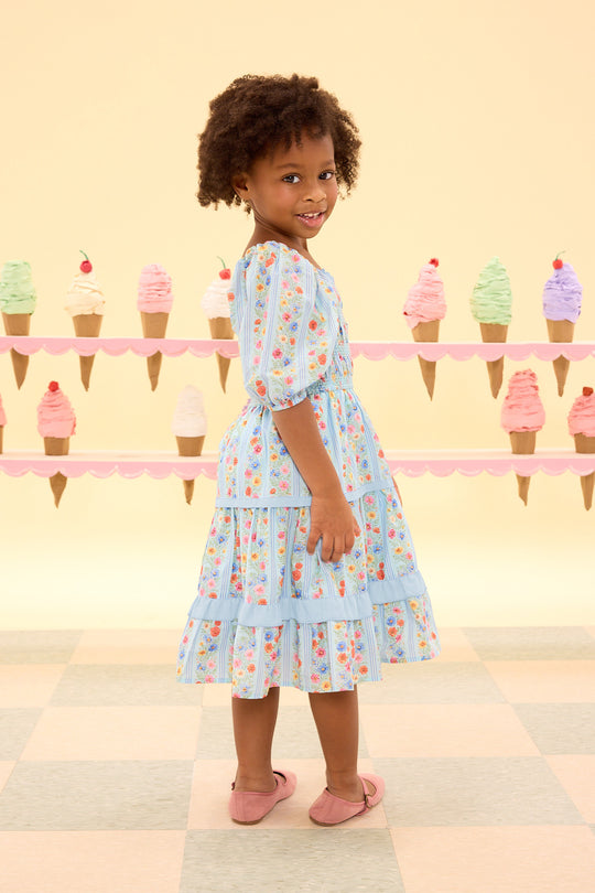 Young girl in a floral dress standing in front of ice cream cone decorations.