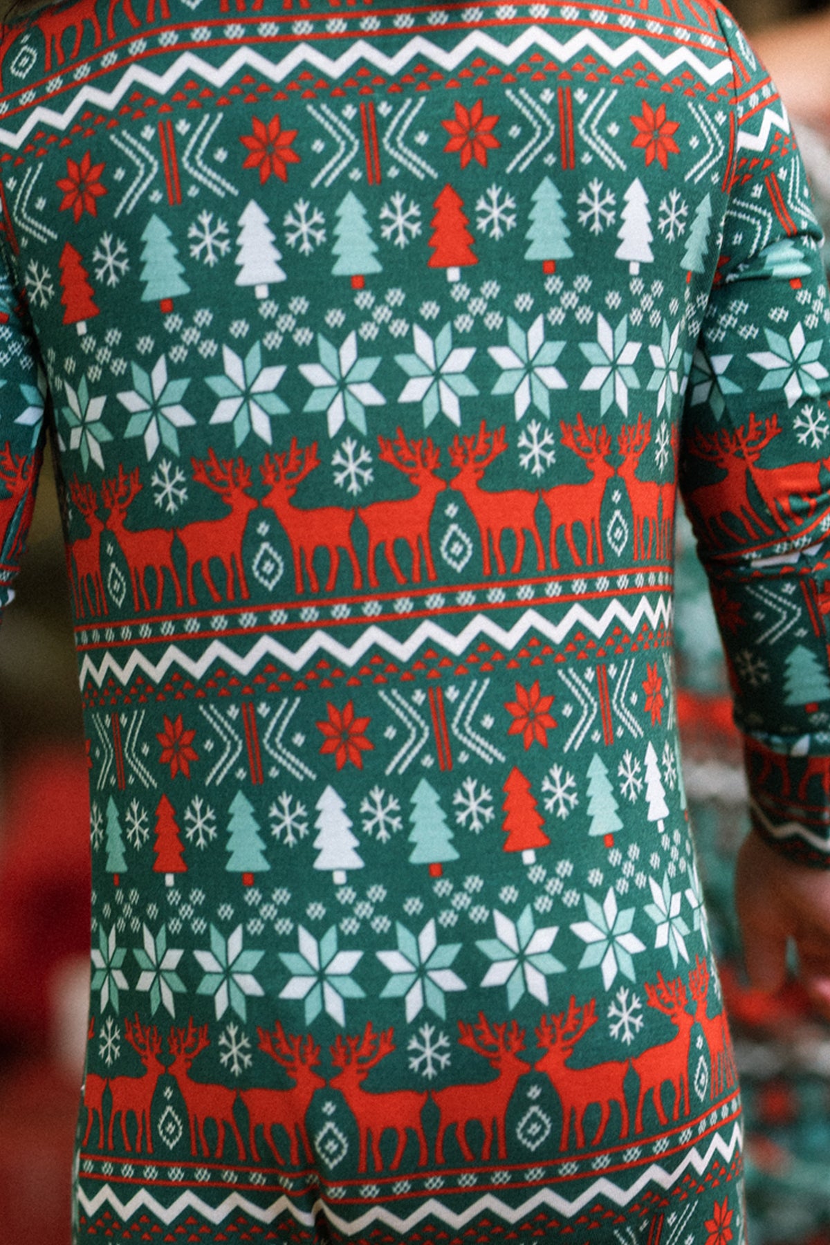 A baby wears the Ivy City Co Baby So Soft Onesie in Alpine Noel—a cozy green, red, and white holiday-themed suit with snowflakes, trees, and reindeer in soft cotton-modal knit.