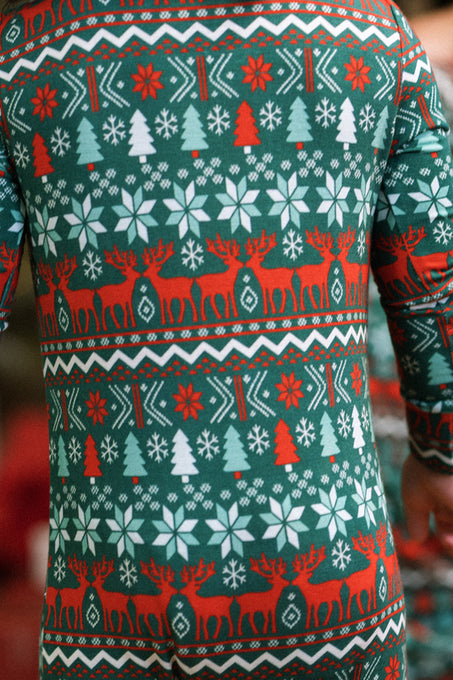 A baby wears the Ivy City Co Baby So Soft Onesie in Alpine Noel—a cozy green, red, and white holiday-themed suit with snowflakes, trees, and reindeer in soft cotton-modal knit.