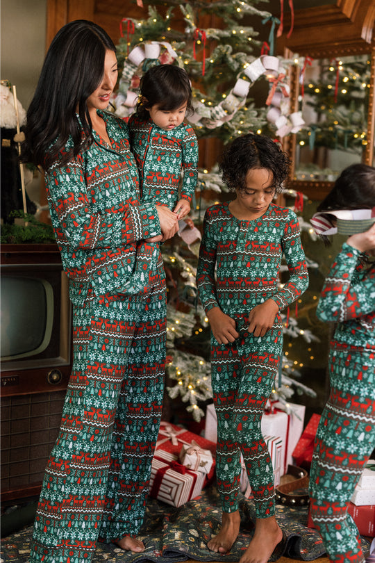 A woman and three children in Ivy City Co’s Baby So Soft Onesie in Alpine Noel pose by a festive tree with gifts and garlands, creating a cozy holiday scene in soft cotton-modal knit.