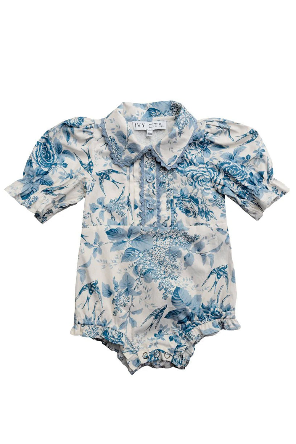 The Baby Sophia Romper in Blue Floral by Ivy City Co features short puff sleeves, a Peter Pan collar, blue floral print on white, cute ruffle and button chest details, and elastic leg openings for comfort.