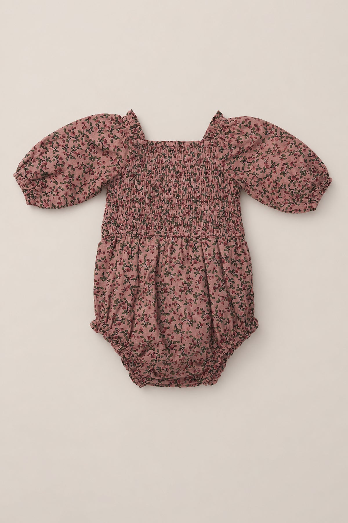 Introducing the Baby Teagan Romper in Mauve Woodland Floral from Ivy City Co—a soft cotton romper featuring a smocked bodice, puffed sleeves, and a charming black and green floral print on a mauve background. Designed with gathered elastic smocking at the chest and waist, this stylish piece lays beautifully flat for an adorable look.
