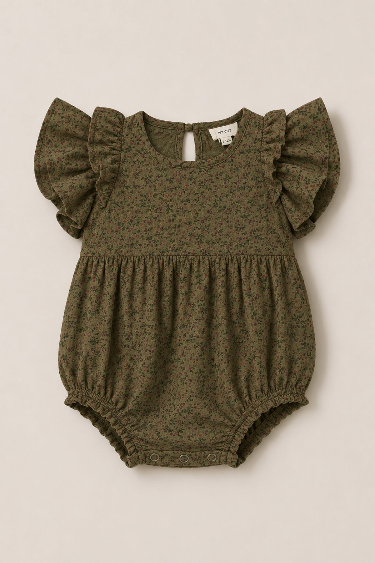 The Baby Hattie Romper in Woodland Floral by Ivy City Co features a charming olive green hue with a delicate floral print, flutter sleeves, a gathered waist, and practical snap closures at the bottom. Crafted from soft cotton, this romper is perfect for providing everyday comfort and style.