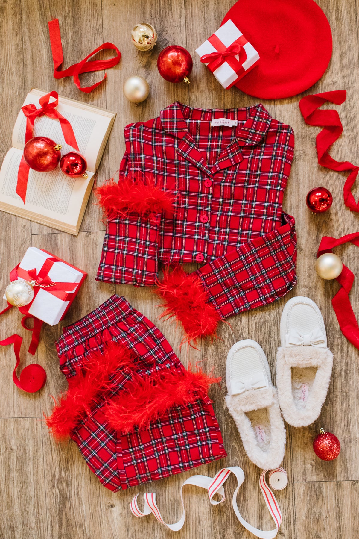 Benjamin Pajama Set in Holiday Plaid with feather trim on the cuffs and hems, arranged with a pair of slippers, wrapped gifts, ornaments, and an open book.