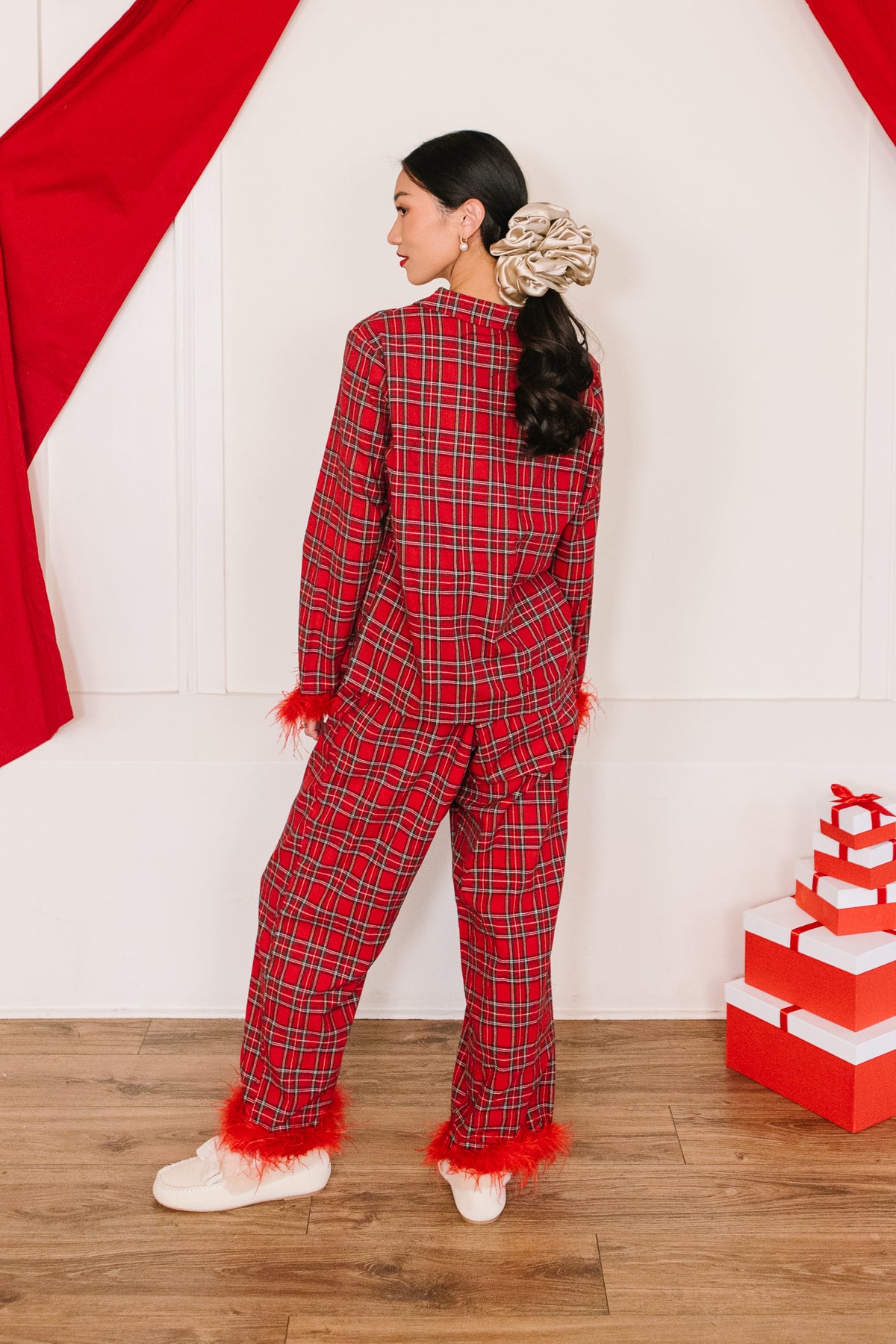 A person seen from behind wearing the Benjamin Pajama Set in Holiday Plaid, a red plaid design with red feather trim at the cuffs and ankles.