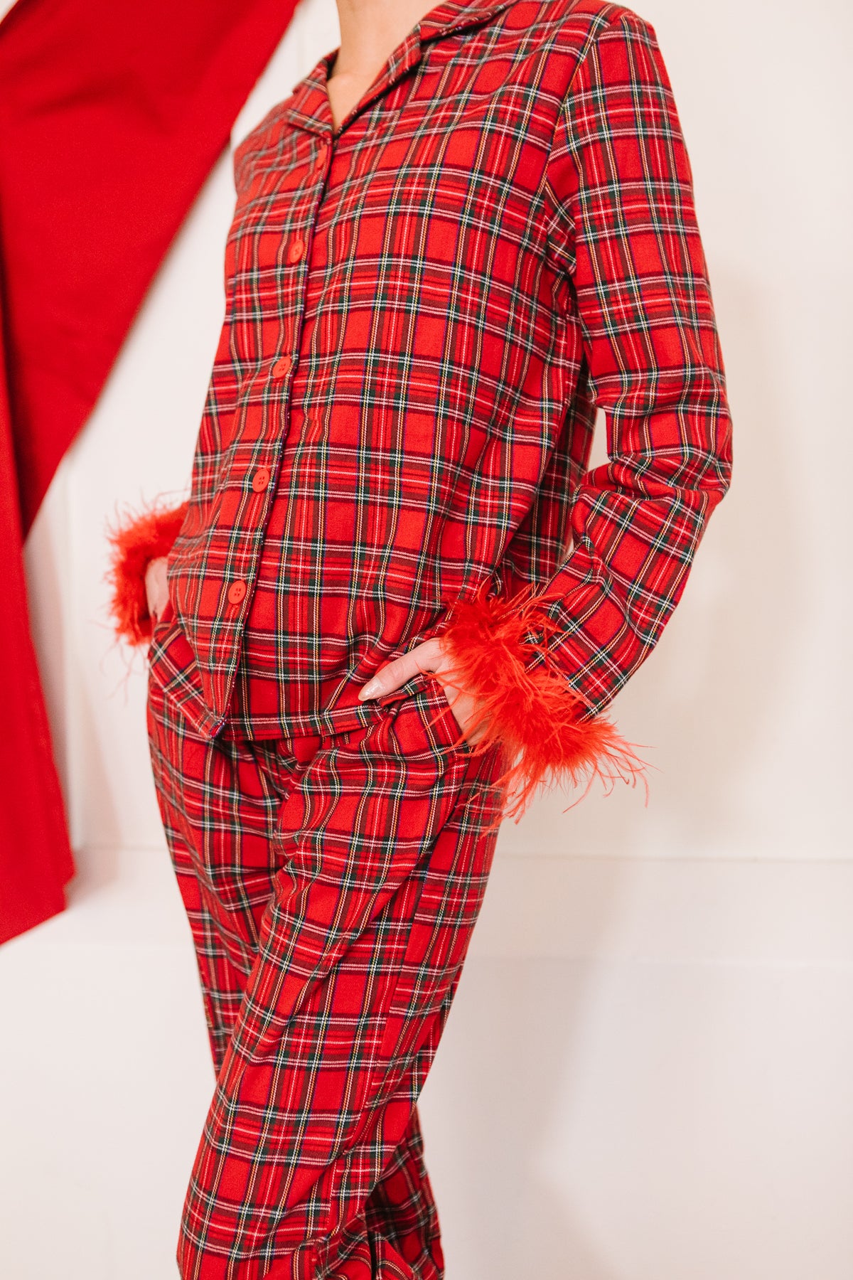 A person wearing an Ivy City Co Benjamin Pajama Set in Holiday Plaid featuring red feather trim on the sleeve cuffs.