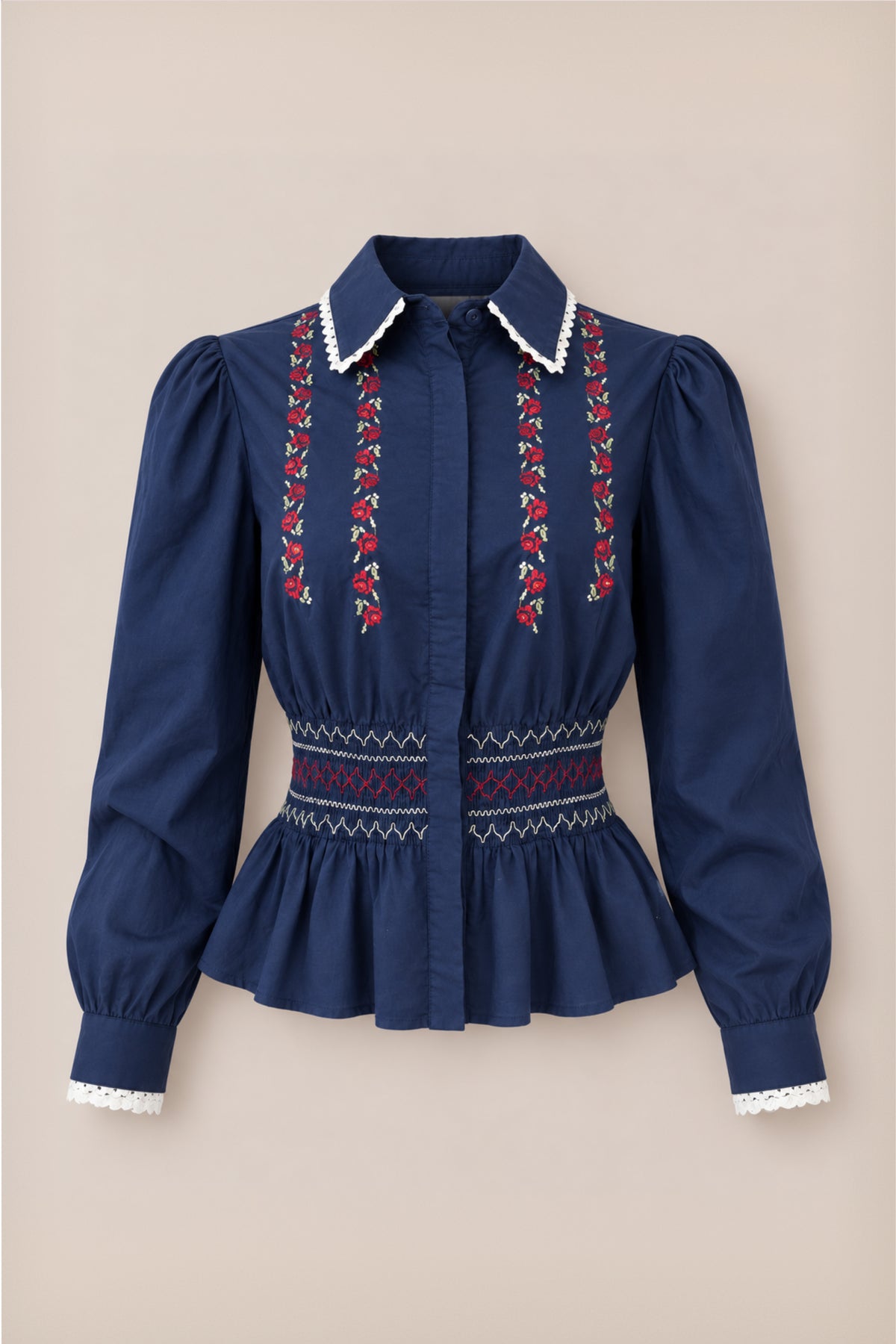 Introducing the Bluebell Top in Sapphire Rosette Embroidery by Ivy City Co—a navy blue girls’ holiday blouse featuring long sleeves with puffed shoulders, elegant white lace trim, and delicate sapphire rosette embroidery on the front. This cotton top showcases a smocked fitted waist, a peplum hem for added charm, a collared neckline, and completed with button closures.
