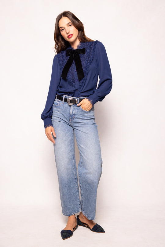 Woman wearing a blue blouse with a black bow and light blue jeans on a white background