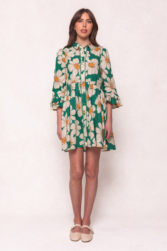A woman stands against a plain background in the Ivy City Co Bowie Dress in Green with White Floral, featuring large white and yellow blooms, three-quarter sleeves, and beige flats—a stylish, nursing-friendly dress that blends comfort and elegance.