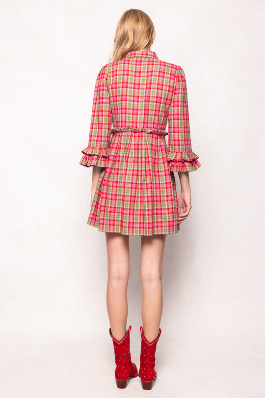 Person wearing a red and green plaid dress with ruffled sleeves on a white background