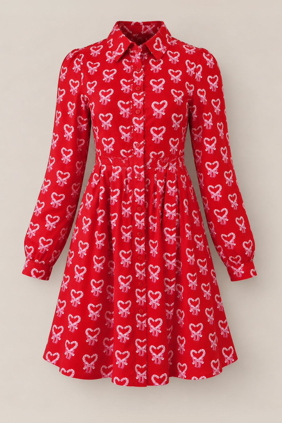 Introducing the Bowie Long Sleeve Dress in Poinsettia Candy Canes by Ivy City Co. This cotton holiday dress features a red base with an all-over print of pink and white candy canes shaped into hearts. Designed with long sleeves, a classic collar, and a button-down front for nursing-friendly wear, it also boasts a slightly pleated skirt. The dress is presented against a plain, light background.