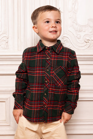 Child wearing a red and black plaid shirt against a decorative white wall.