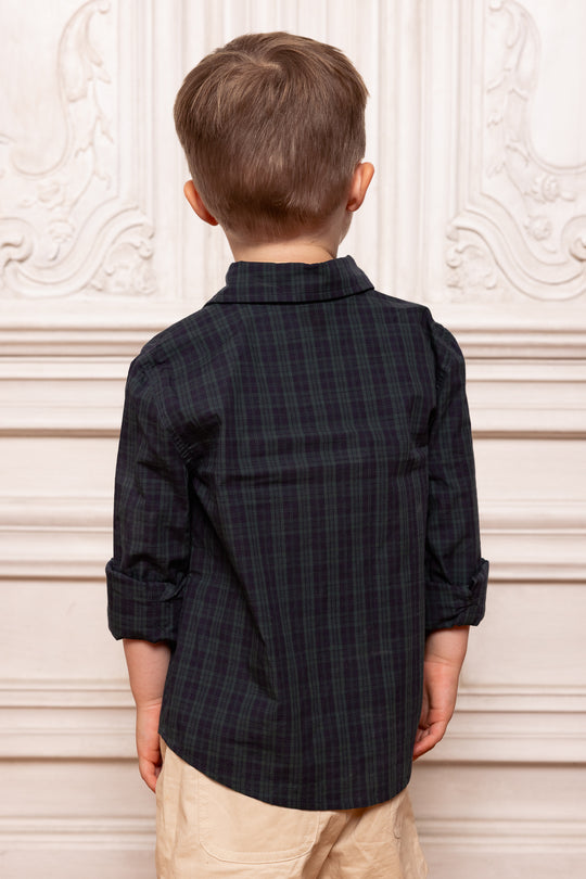 Child wearing a black plaid shirt against a decorative white wall.