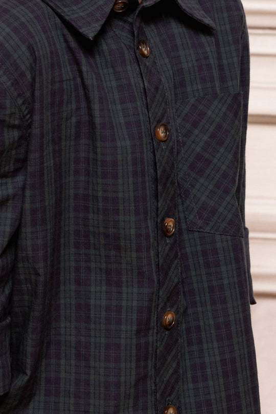 Close-up of a dark plaid coat with brass buttons on a neutral background