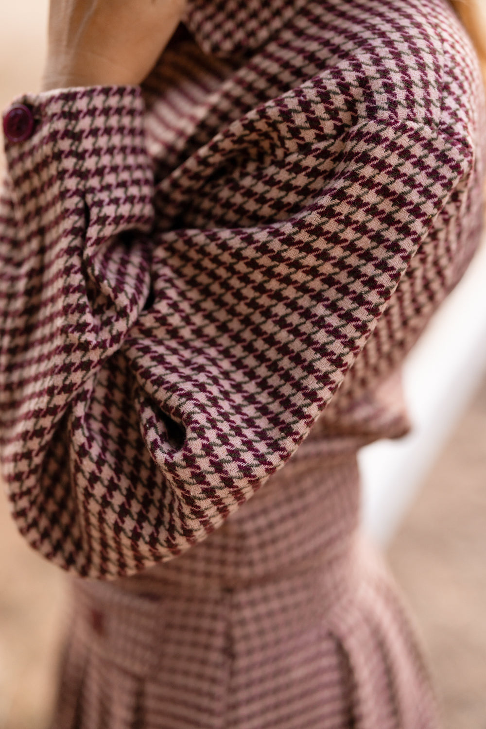 A close-up of a person wearing the Ivy City Co Bradley Jacket in Mauve Houndstooth, featuring ruffled sleeves and a bold purple and pink houndstooth pattern, with their arm bent toward their head. This nursing-friendly jacket beautifully blends eye-catching style with practical functionality.