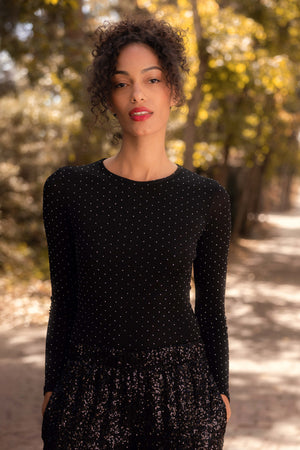 Woman wearing a black long-sleeve top with a pattern, standing outdoors with trees in the background.
