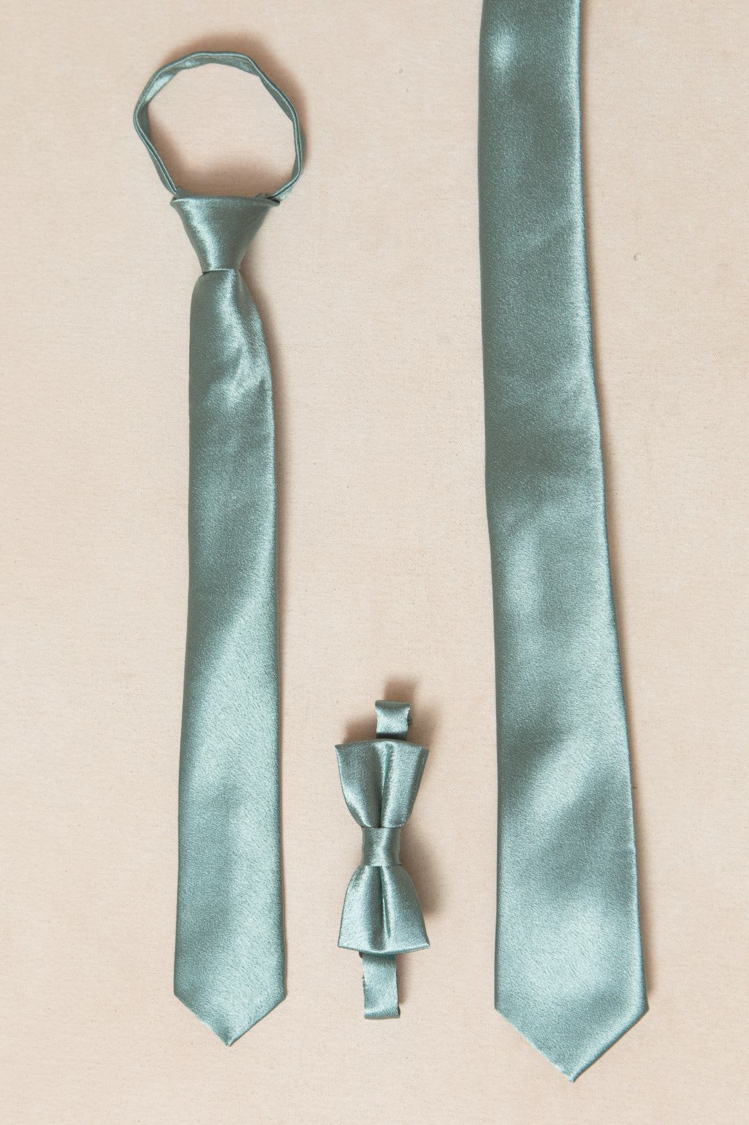 Three light green "Seaglass Satin" tie accessories by Ivy City Co are shown on a beige surface: a pre-tied necktie, a traditional Mens Max Tie, and a bow tie.