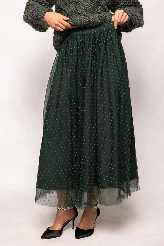 Person wearing a dark green polka dot skirt with a plain background