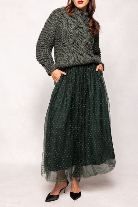 Woman wearing a green knitted sweater and a long green skirt with a white background