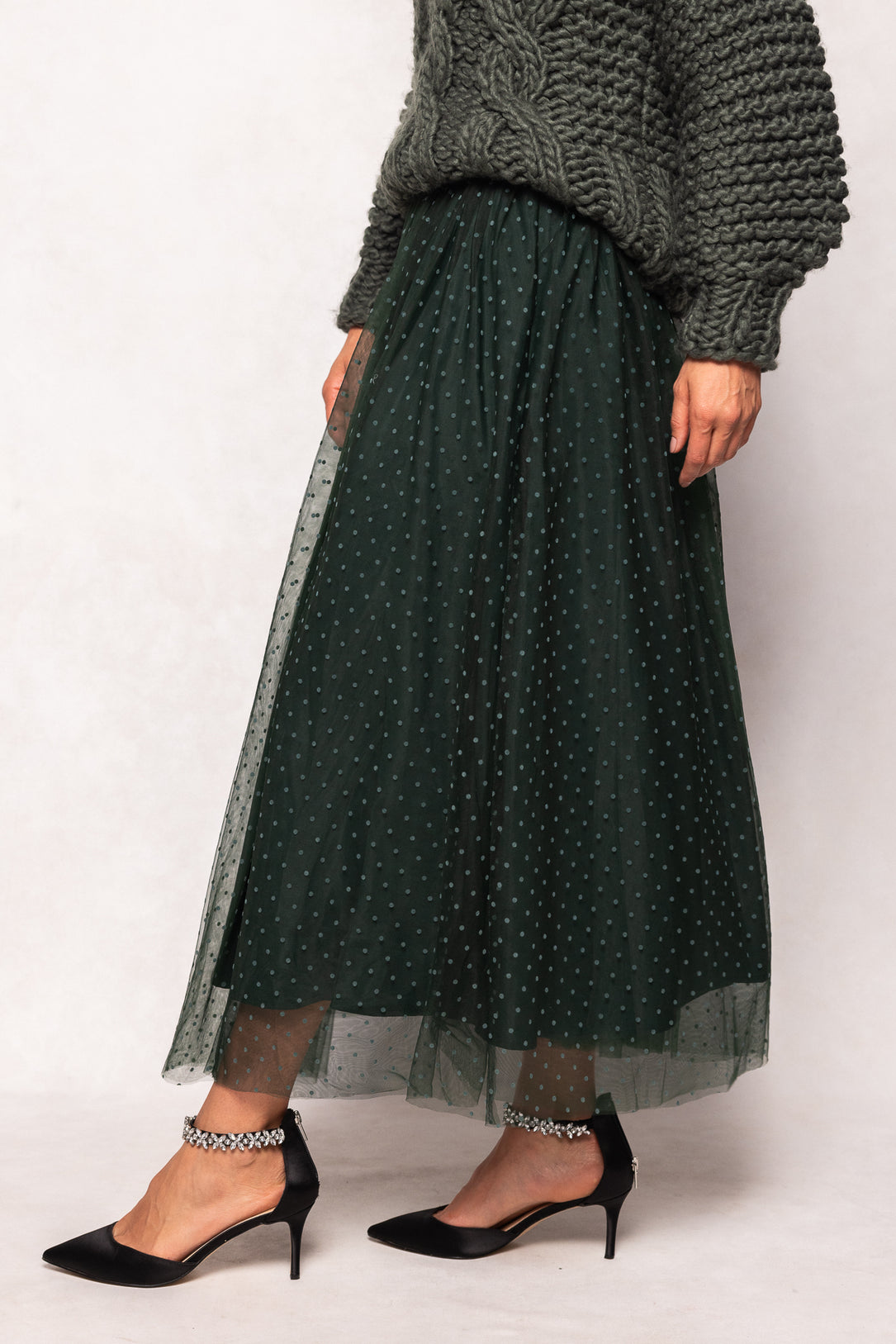 Person wearing a dark green polka dot skirt with a gray sweater on a white background