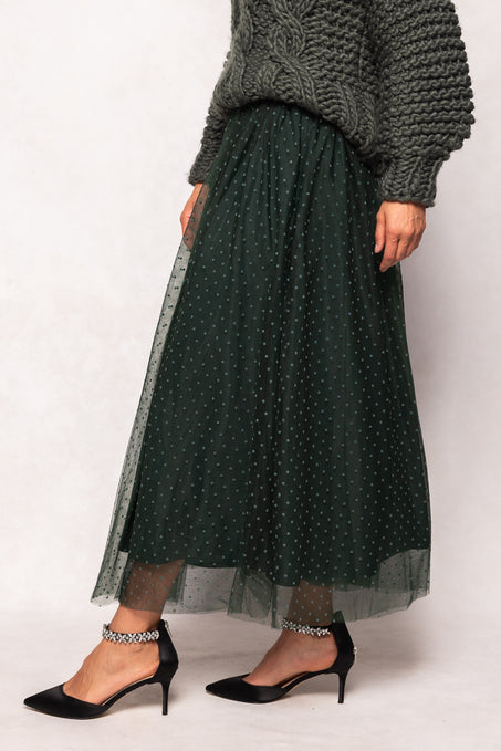 Person wearing a dark green polka dot skirt with a gray sweater on a white background
