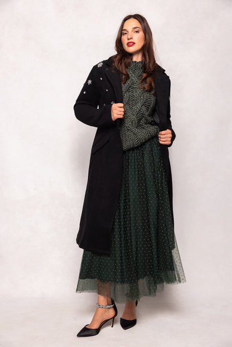 Woman wearing a long black coat over a green dress on a white background