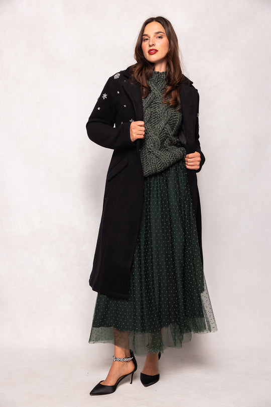 Woman wearing a long black coat over a green dress on a white background