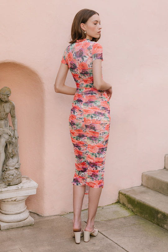 A woman stands outdoors near stone steps, wearing the Ivy City Co Brynn Short Sleeve Dress in Multicolor Floral with nude heeled sandals. A classical statue is on the left, and a pale pink wall is behind her.