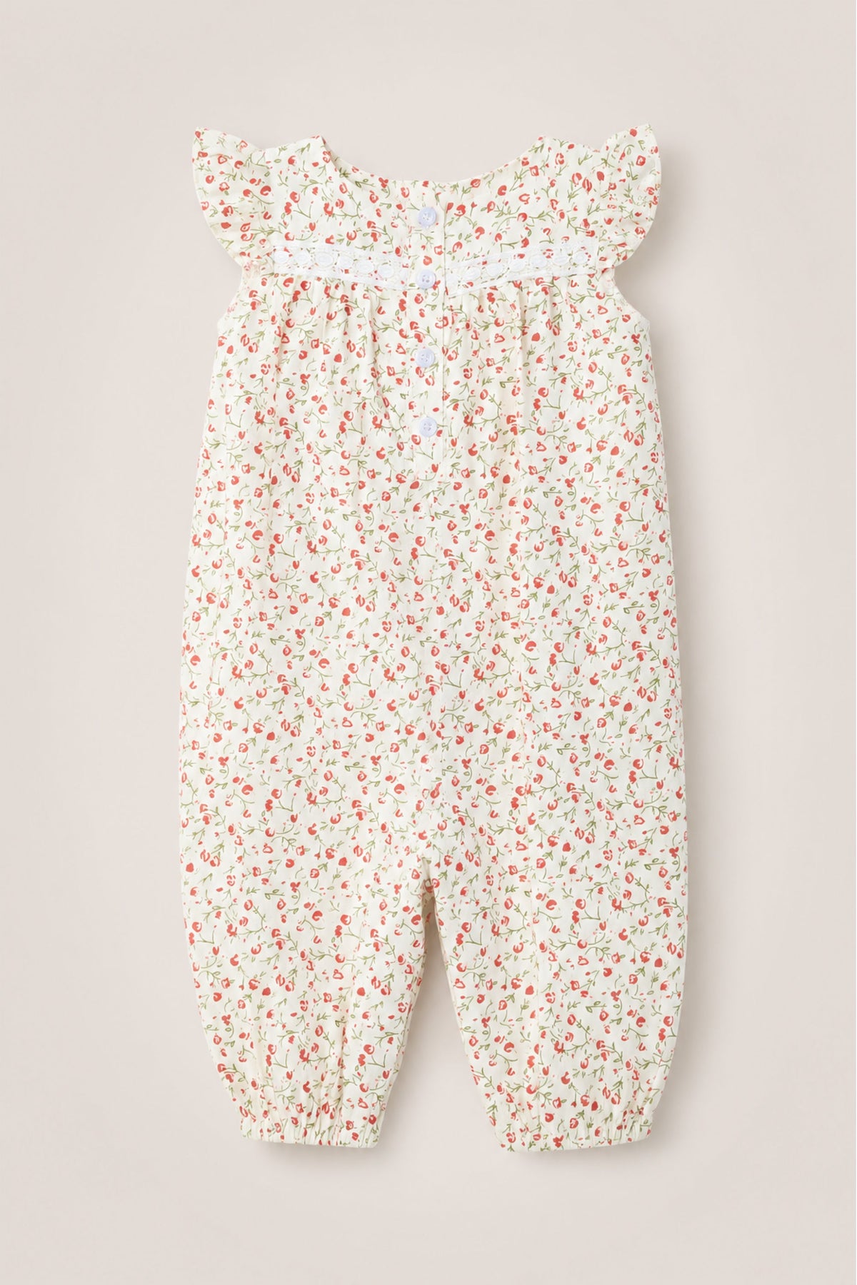The Ivy City Co Baby Mirabelle Romper in Cream Ditsy Floral features a small red and green floral print on a soft cream background. This adorable cotton romper is designed with ruffled cap sleeves, delicate smocking across the chest, gathered cuffs at the ankles, and charming lace trim. Its loose fit ensures all-day comfort, making it a sweet choice for your little one.