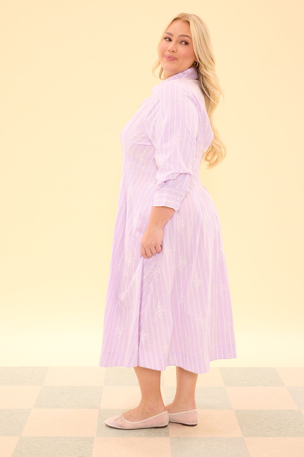 Woman wearing a light purple striped dress on a checkered floor with a beige wall background