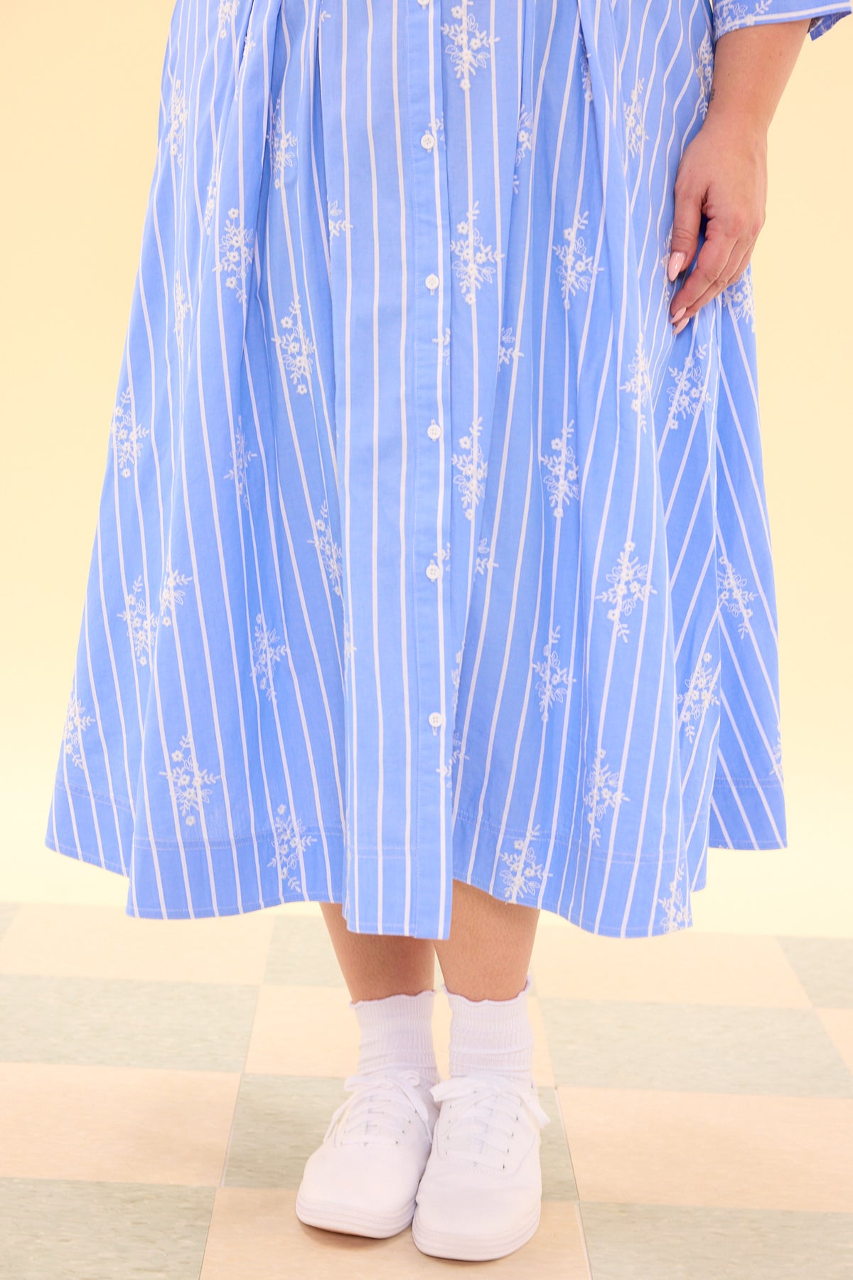 Person wearing a blue and white striped dress with floral patterns on a beige background
