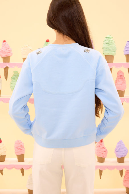 Person wearing a light blue sweatshirt with decorative buttons in front of a colorful ice cream cone display.