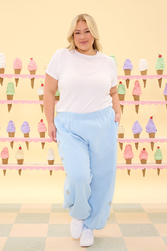 Woman wearing a white t-shirt and light blue sweatpants standing in front of a wall with ice cream cone decorations.