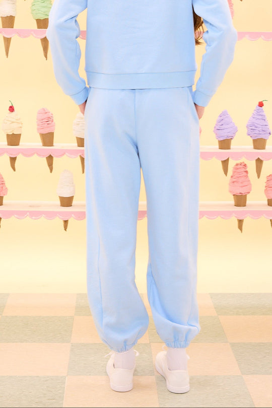 Person wearing a light blue outfit standing in front of a wall with ice cream cone patterns.