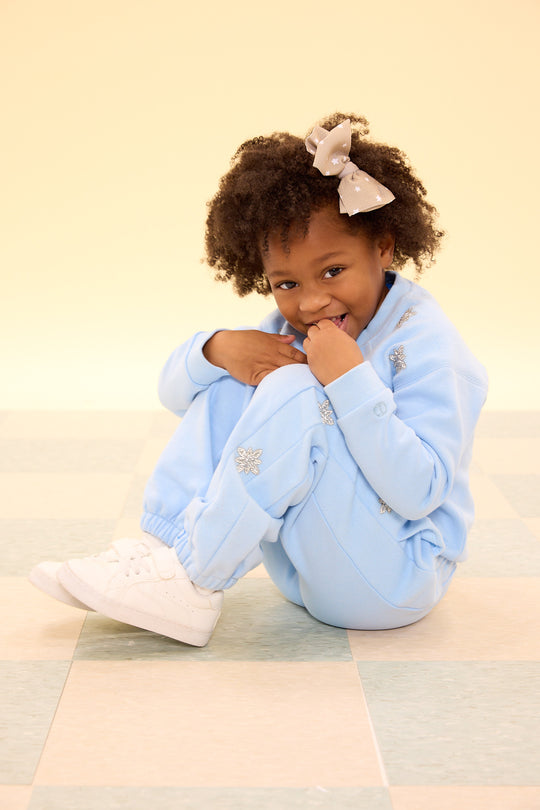 Child wearing a light blue outfit sitting on a checkered floor.