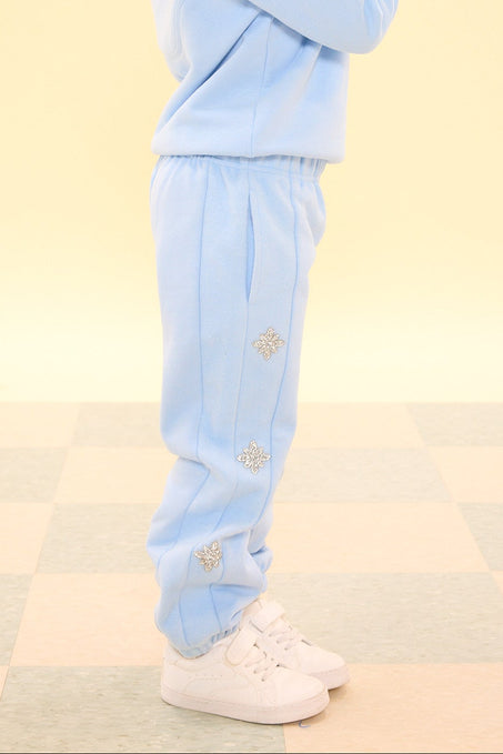 Child wearing a light blue tracksuit pointing upwards on a checkered floor.