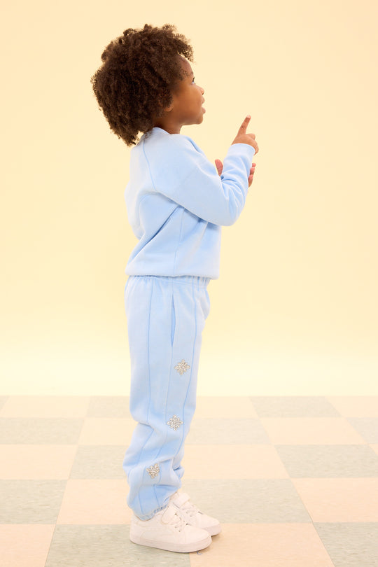 Child wearing a light blue tracksuit pointing upwards on a checkered floor.