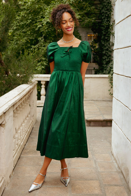 Woman in a green dress standing outdoors on a stone path with greenery in the background
