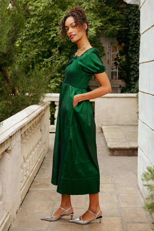 Woman in a green dress standing on a stone path with greenery in the background