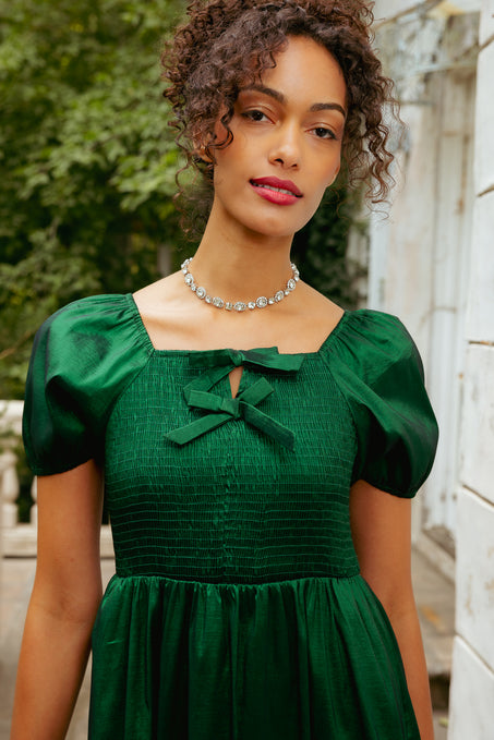 Woman wearing a green dress with puffed sleeves and a bow detail, standing outdoors.