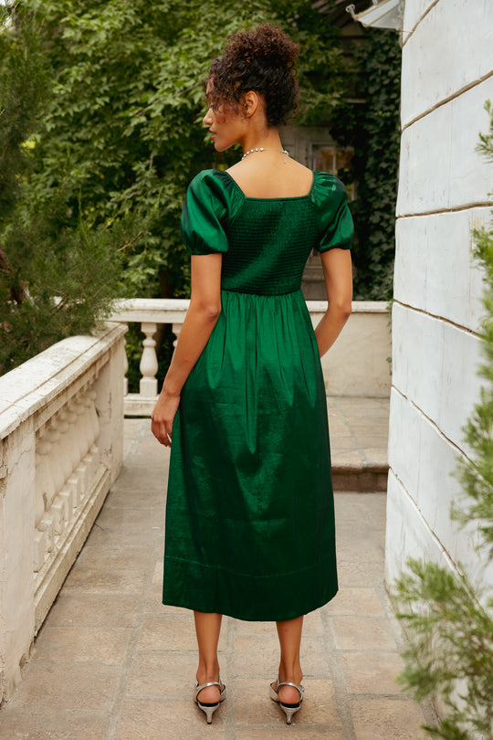 Woman in a green dress standing on a stone path with greenery in the background