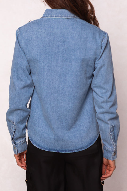 A person is seen from the back wearing the Ivy City Co Rhinestone Cowboy Shirt—a light blue denim jacket with long sleeves and jewel embellishments—paired with black pants, standing against a plain light background.