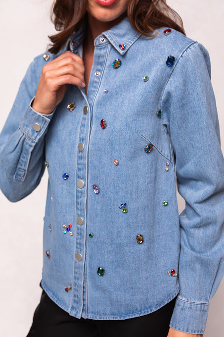 A person wears the Ivy City Co Rhinestone Cowboy Shirt in light blue denim with jewel embellishments and silver buttons, one hand touching the collar. Their face is partially out of frame.