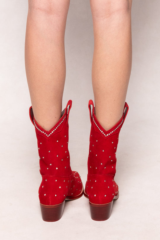 Red cowboy boots with rhinestone details worn by a person on a light gray background