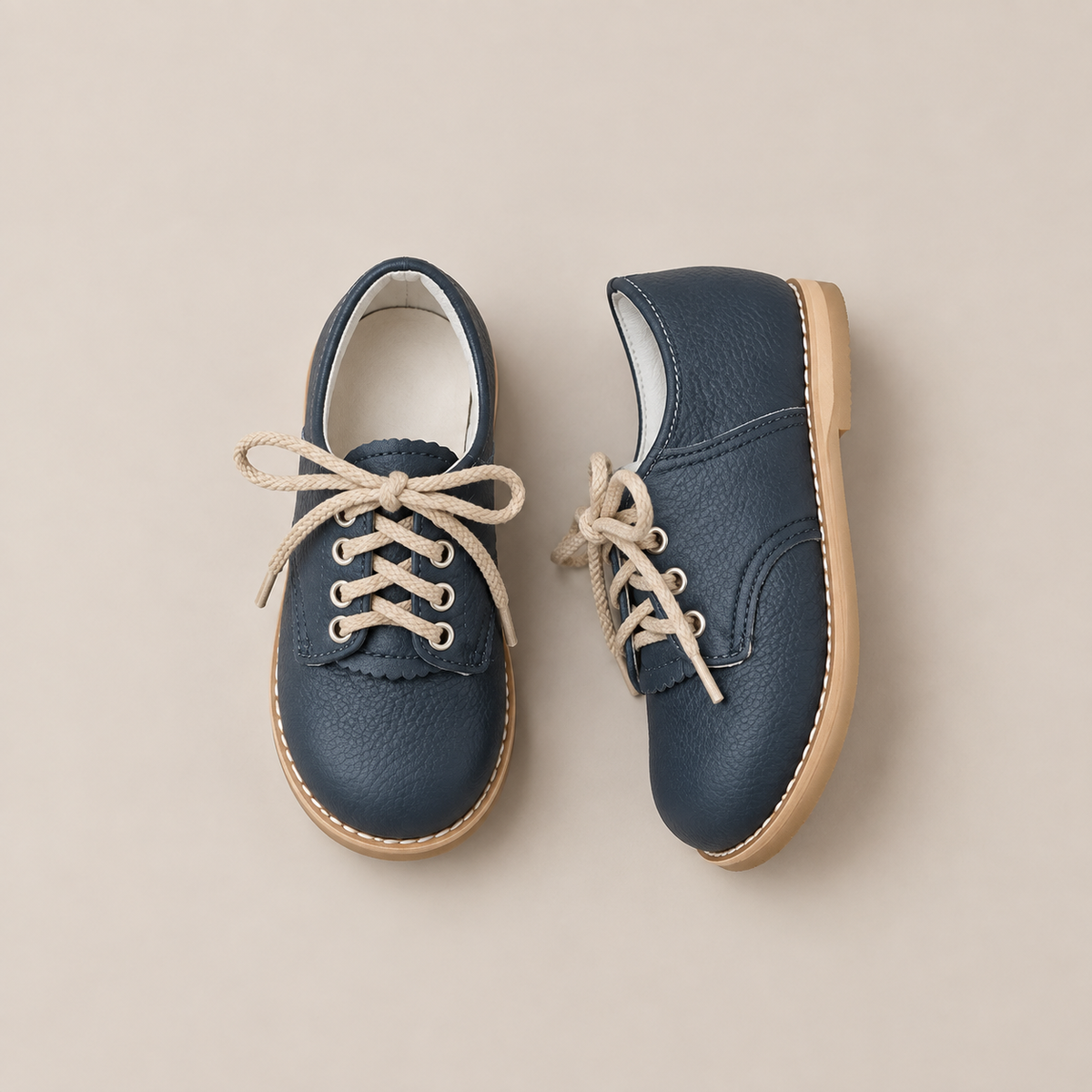The Mini Boys Saddles in Navy by Zimmerman Shoes are a pair of small navy leather saddle shoes for children, featuring a stylish fringe tongue, tan laces, and light brown soles. Displayed on a neutral background, they are perfect for formal events.