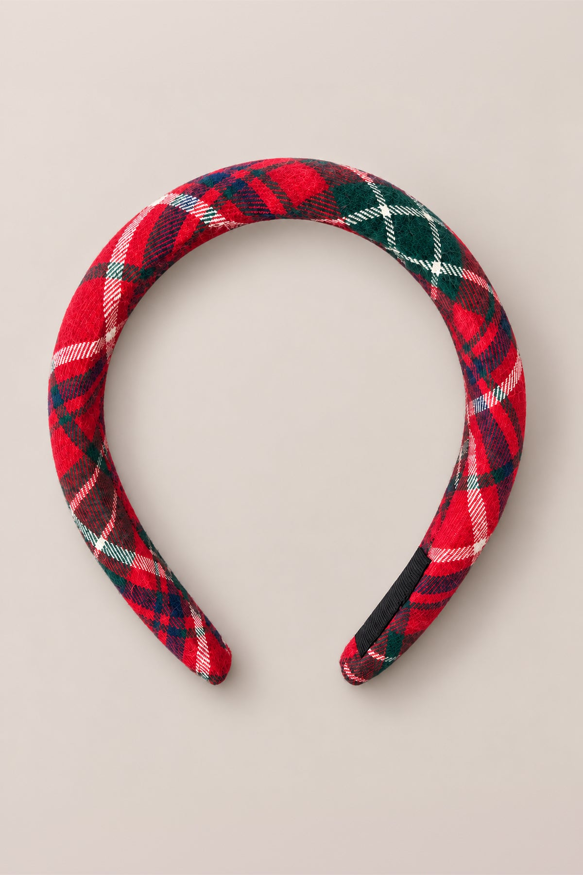 The Ivy City Co “Hair Bows in Christmas Cheer Plaid” headband, padded for comfort and covered in red, green, white, and navy plaid fabric, is displayed against a simple beige background—making it an ideal accessory for festive holiday photos.